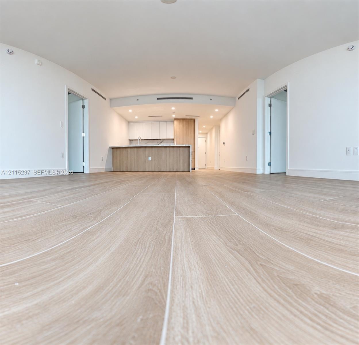 Open-concept interior featuring light wood-finish flooring, recessed lighting, and a kitchen island with stone-finish countertops and wood-grain cabin