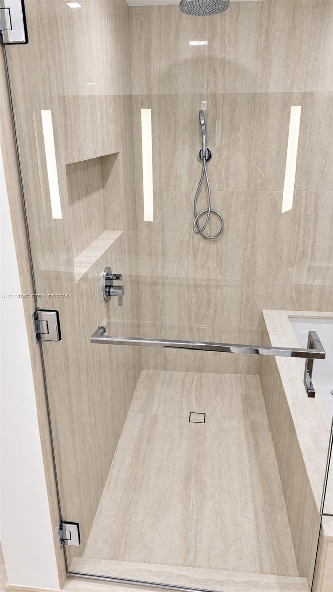 Walk-in shower featuring natural-stone tile surrounds, a rain-style showerhead with a handheld attachment, a built-in recessed niche, and a frameless 