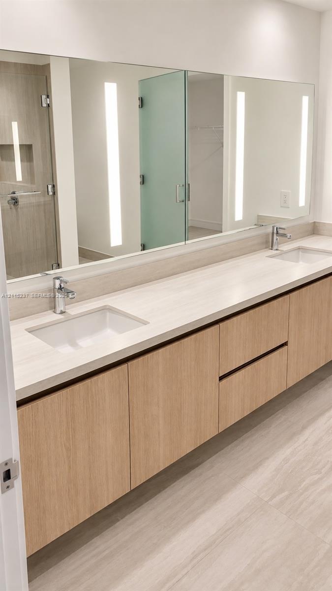 Floating wood-finish vanity with dual integrated rectangular sinks, light-toned stone-finish countertop, integrated linear vertical LED mirror lightin