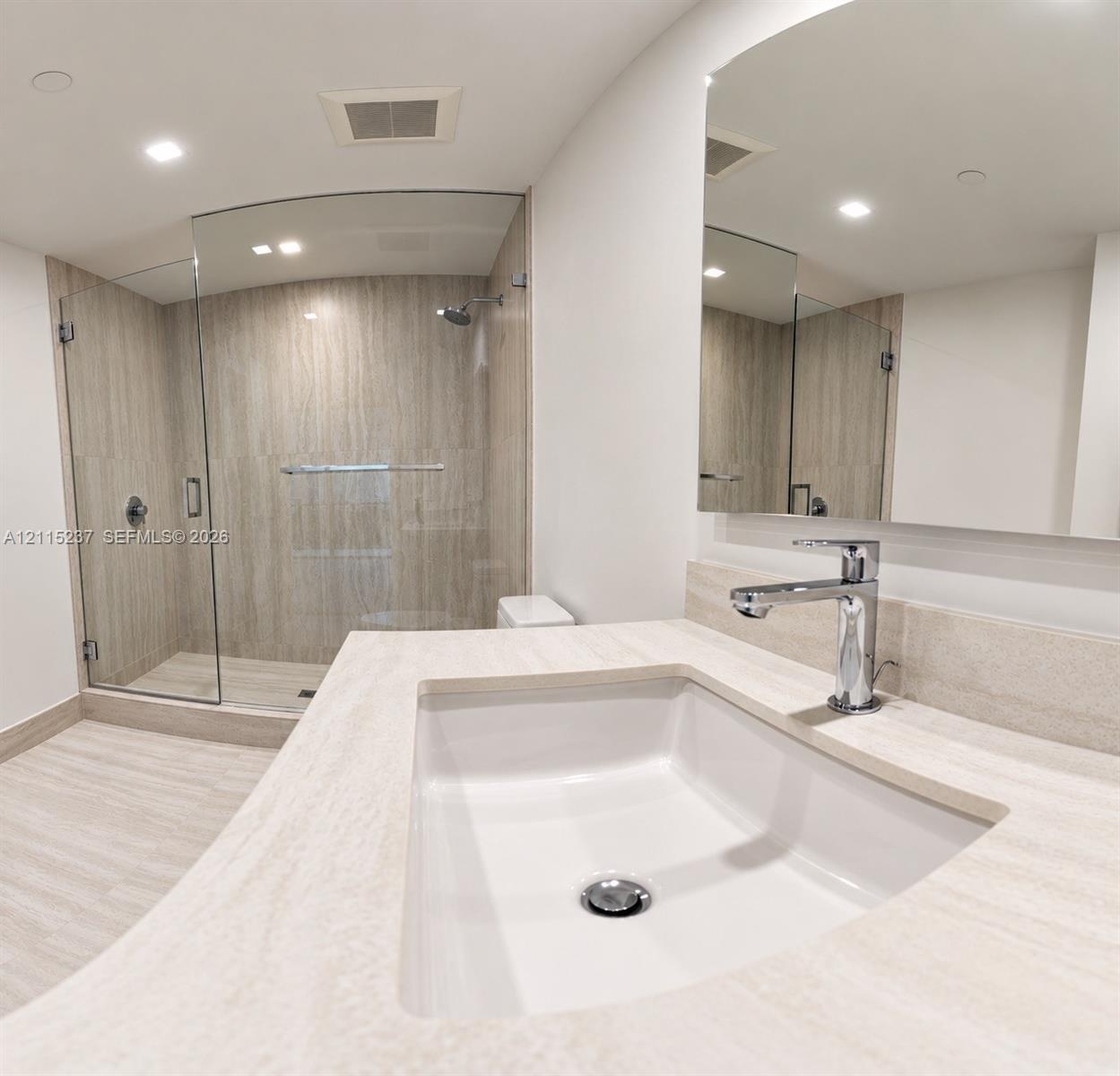 Bathroom featuring a vanity with an integrated rectangular sink and polished chrome faucet, stone-finish countertop, frameless glass shower enclosure,