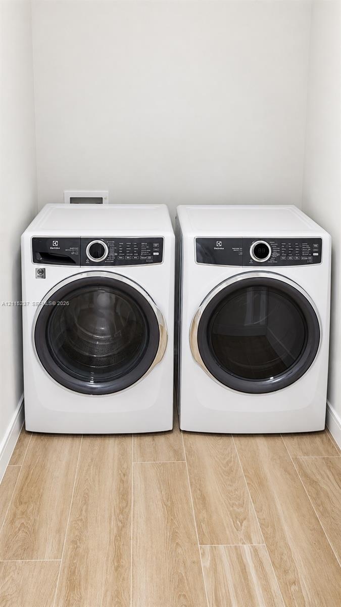 Laundry area featuring front-loading washer and dryer units set upon wood-finish flooring