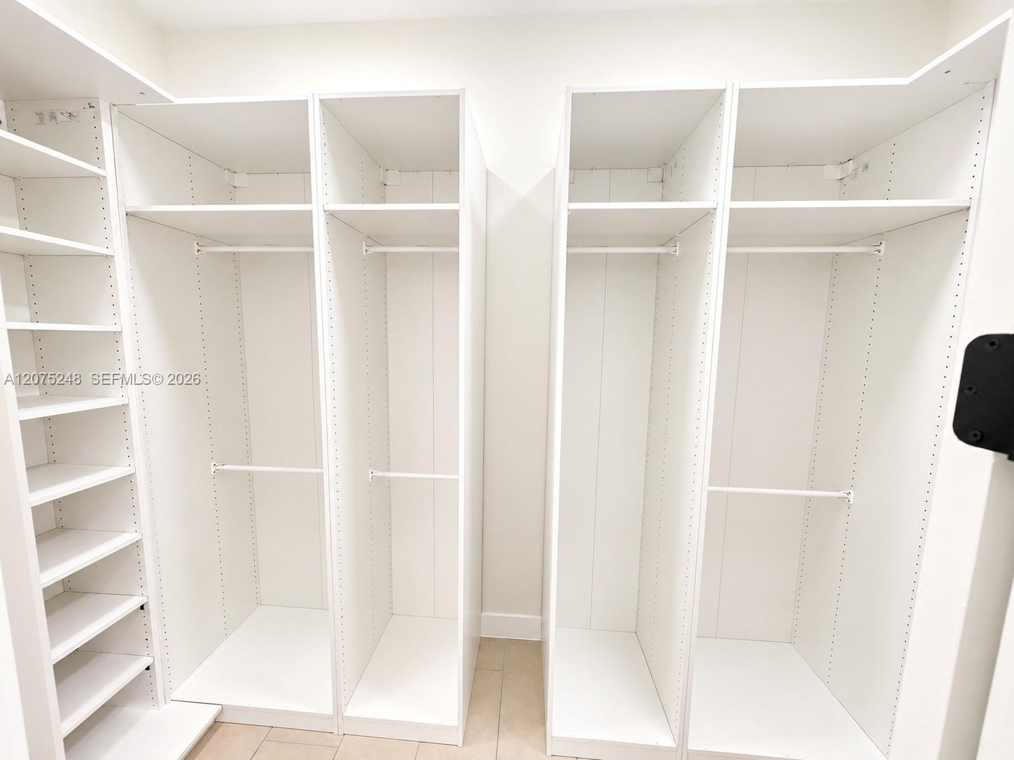 Custom walk-in storage featuring white built-in cabinetry, adjustable shelving, integrated garment rods, and tiled flooring