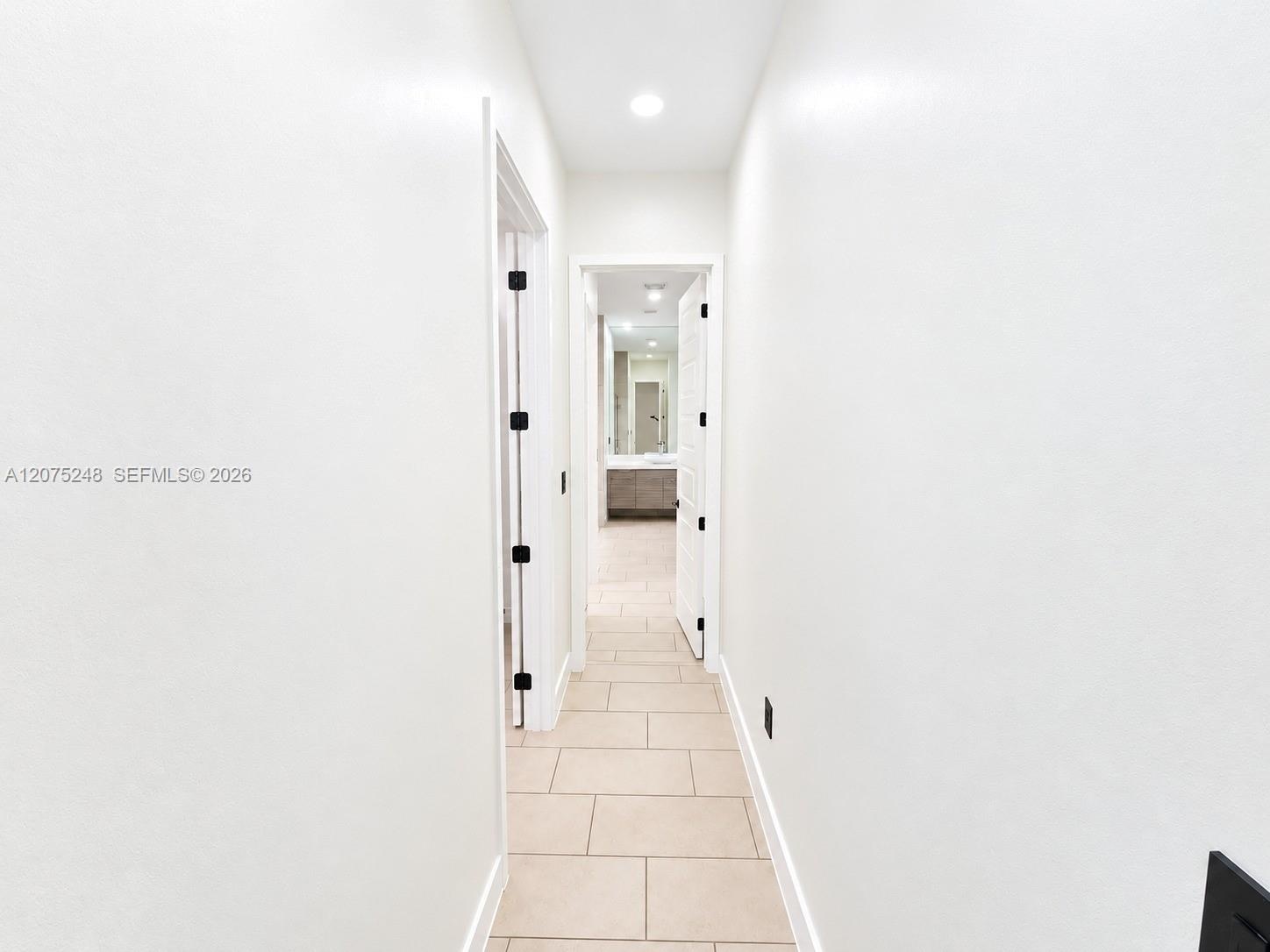 Hallway featuring light-toned tile flooring, recessed ceiling lighting, and solid core doors with matte black hardware