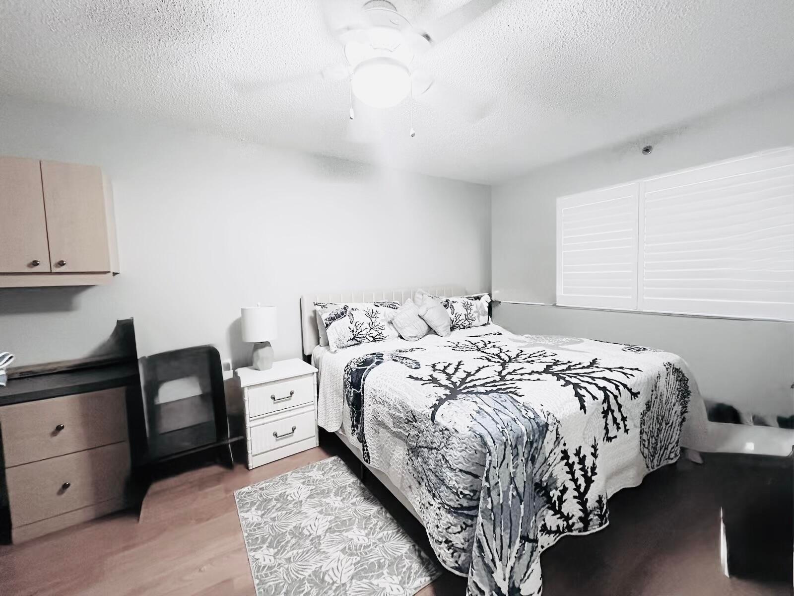 Bedroom featuring wood-finish flooring, a ceiling fan with integrated lighting, and plantation shutters