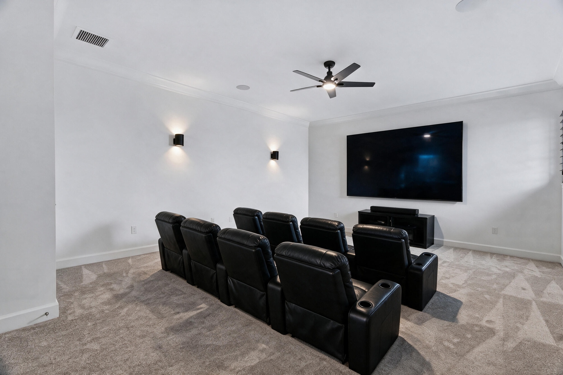 Media room featuring neutral carpeting, a ceiling-mounted fan, dual wall-mounted sconces, and recessed ceiling lighting