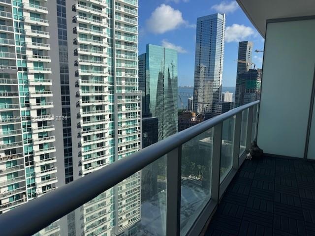 Covered balcony featuring square interlocking floor tiles and a full-height glass railing with a metallic handrail