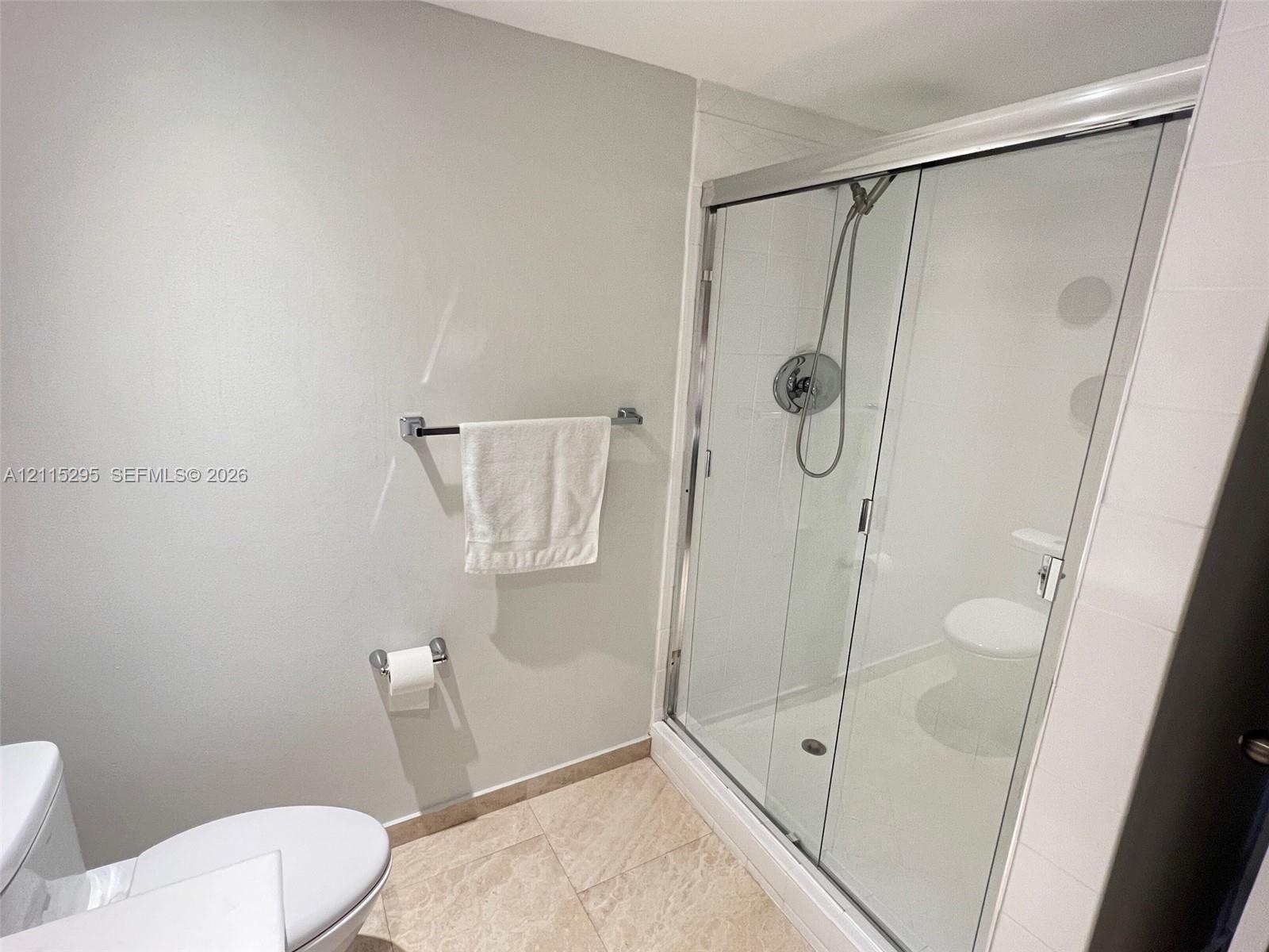 Walk-in shower with sliding glass doors, adjustable handheld shower fixture, light-toned tile flooring, and wall-mounted chrome hardware