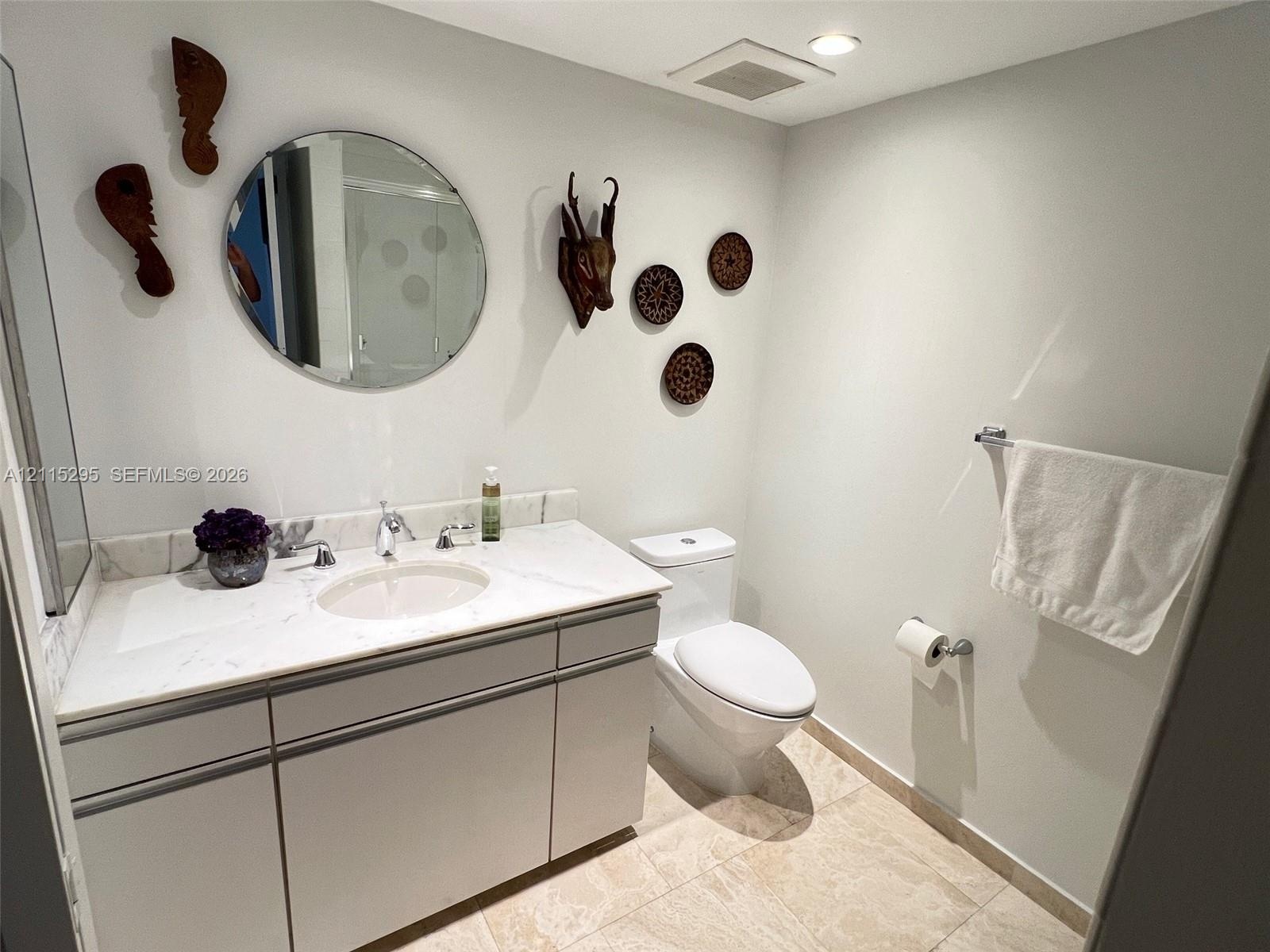 Bathroom featuring a vanity with stone-top surfacing, undermount basin, circular wall mirror, polished chrome fixtures, and tile flooring
