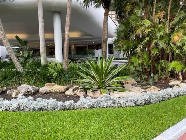Landscaped garden featuring mature palm trees, decorative rock borders, and manicured turf grass under a curved structural overhang supported by white