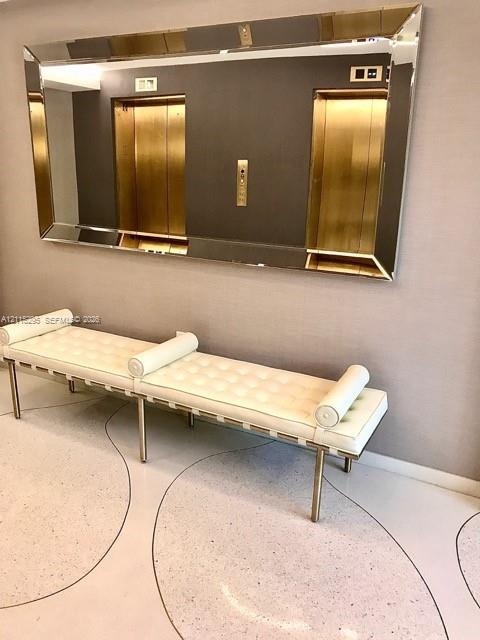 Dual elevator bank featuring metallic gold doors, wall-mounted control panel, large rectangular decorative mirror with beveled edges, and polished ter