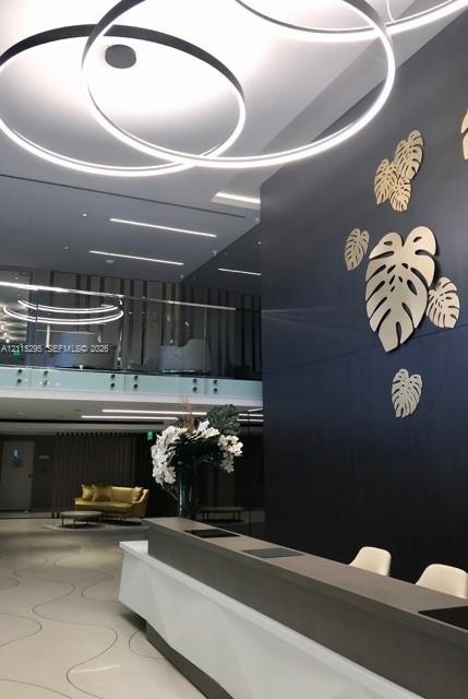 Lobby featuring a tiered, sculptural reception desk with a white matte finish, circular pendant lighting, polished stone flooring with inlaid curvilin