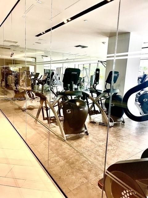 Fitness room featuring wall-to-wall mirrors, neutral tile flooring, and recessed ceiling lighting