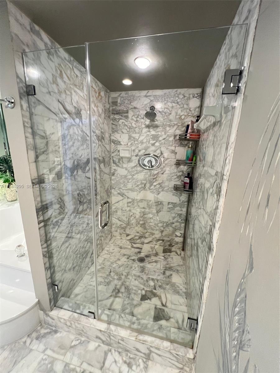 Walk-in shower with floor-to-ceiling natural stone tile, frameless glass enclosure, polished chrome hardware, and recessed lighting