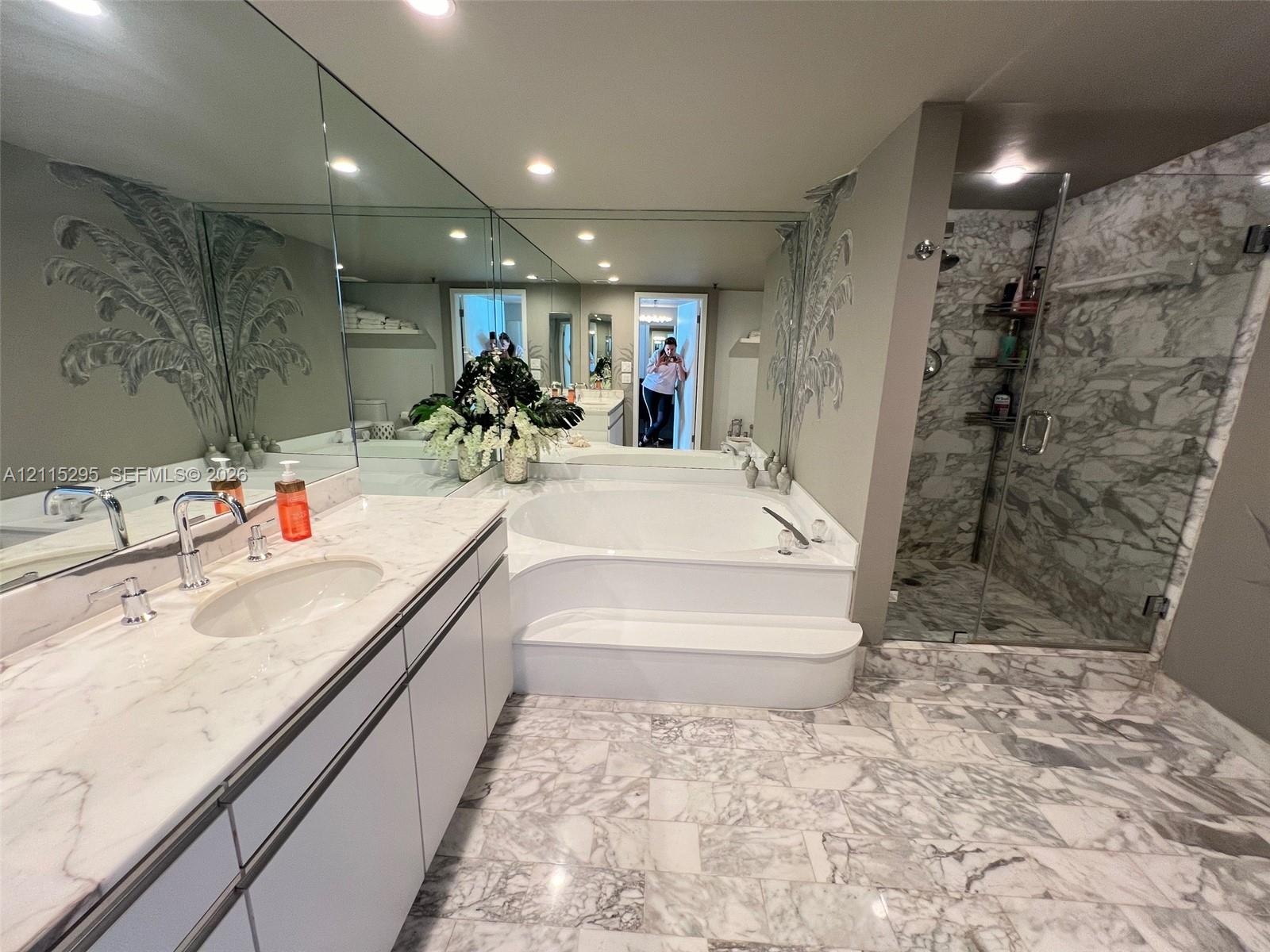 Bathroom featuring a stone vanity countertop with an integrated oval sink, full-width wall mirror, oversized soaking tub with a stepped entry, and a w