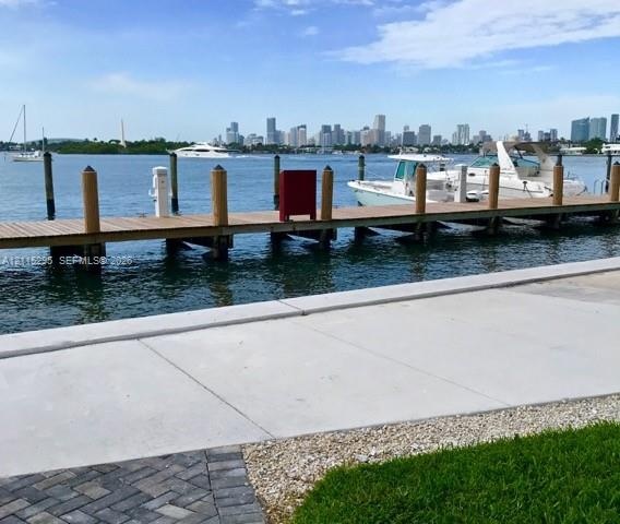 Private dock with wood planking and piling, concrete bulkhead, paved walkway, and manicured turf
