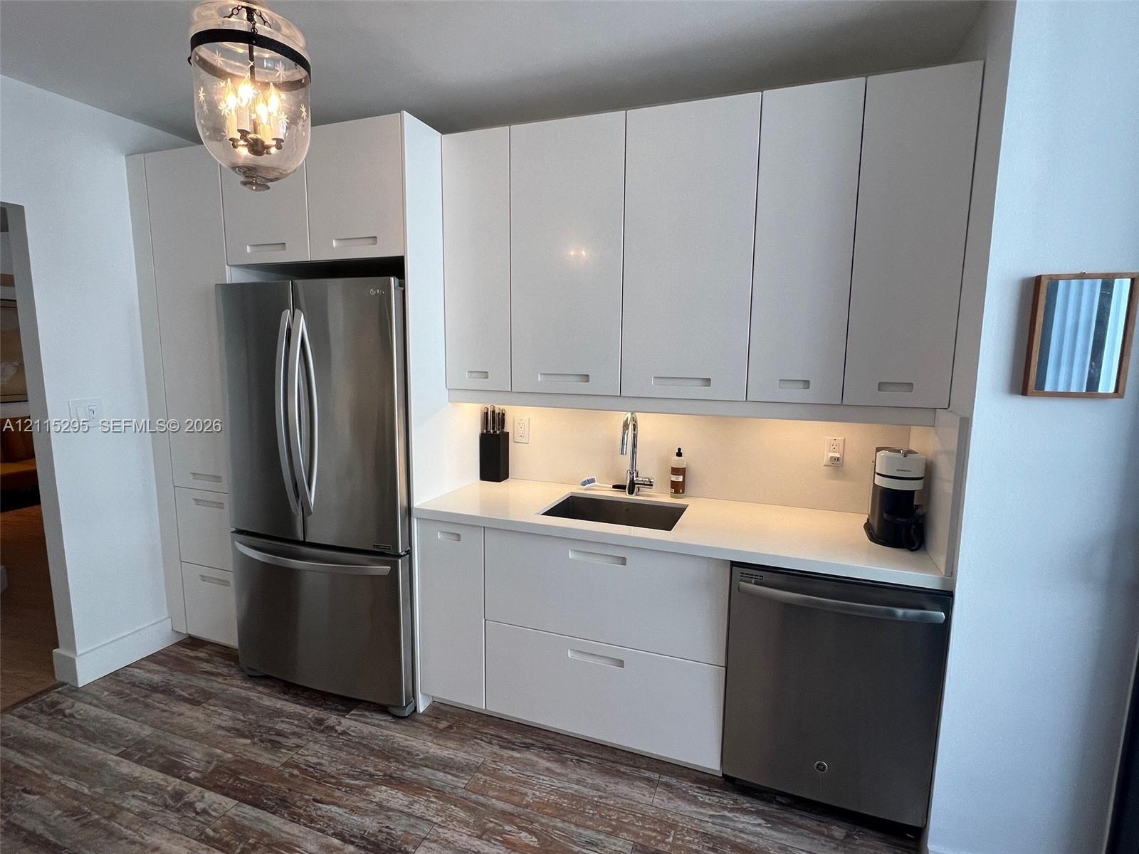 Kitchen area featuring flat-panel white cabinetry, solid-surface countertops, integrated stainless steel appliances, undermount sink with a gooseneck 