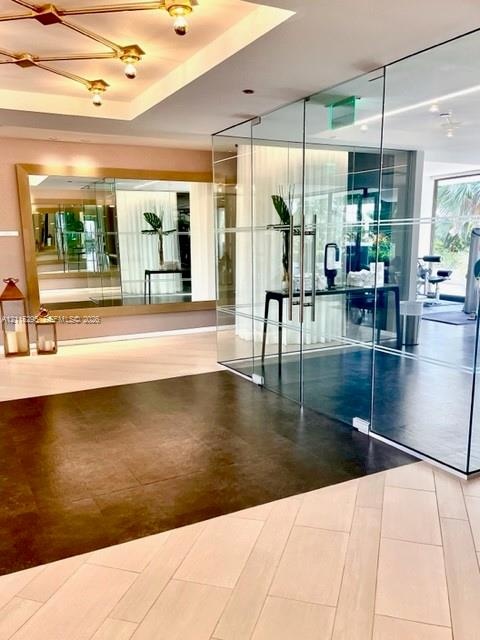 Floor-to-ceiling glass enclosure with stainless steel hardware, gold-tone geometric ceiling lighting, large-format wall mirror, and contrasting tile f