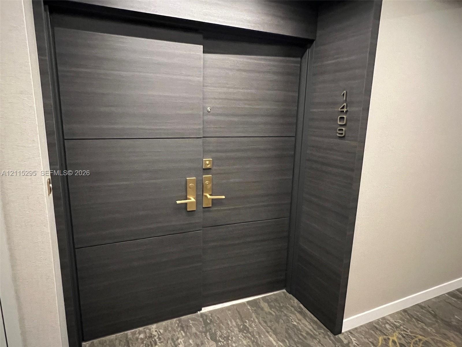 Dark-toned, horizontal-grain double entry door featuring brushed metal hardware and integrated unit numbering