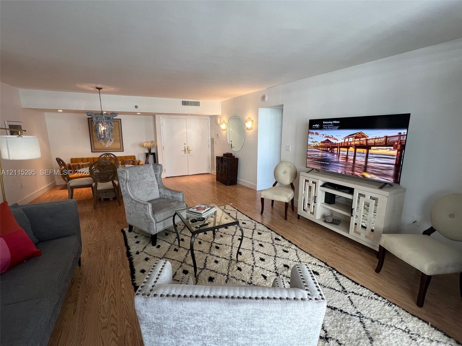 Open-concept interior featuring light-tone wood-finish flooring, decorative wall-mounted lighting fixtures, and a recessed ceiling chandelier