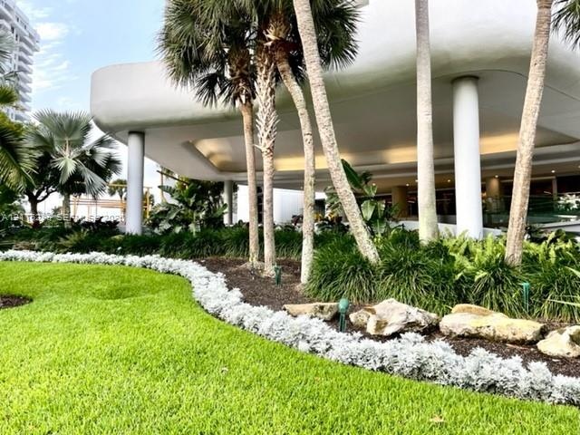 Mid-century modern architectural overhang featuring structural pillars, mature palm trees, tiered stone landscape edging, and manicured lawn