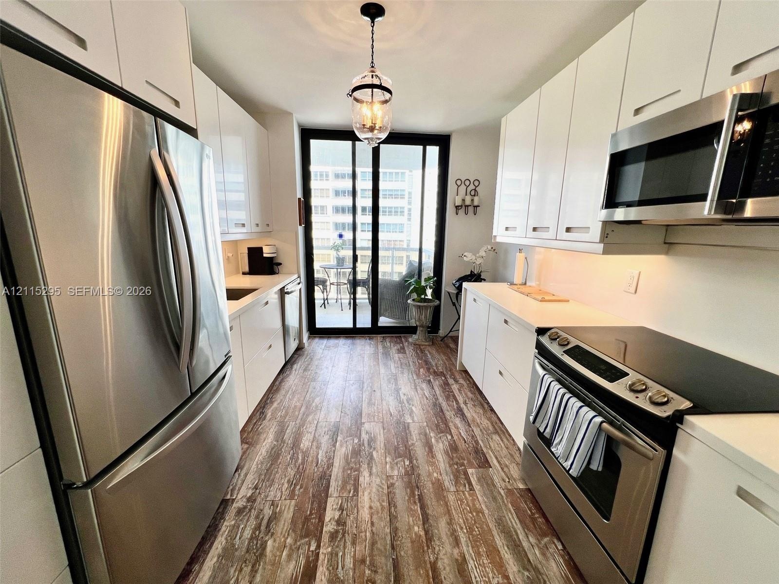 Galley kitchen featuring white high-gloss cabinetry, stainless steel appliances, wood-finish flooring, and sliding glass doors