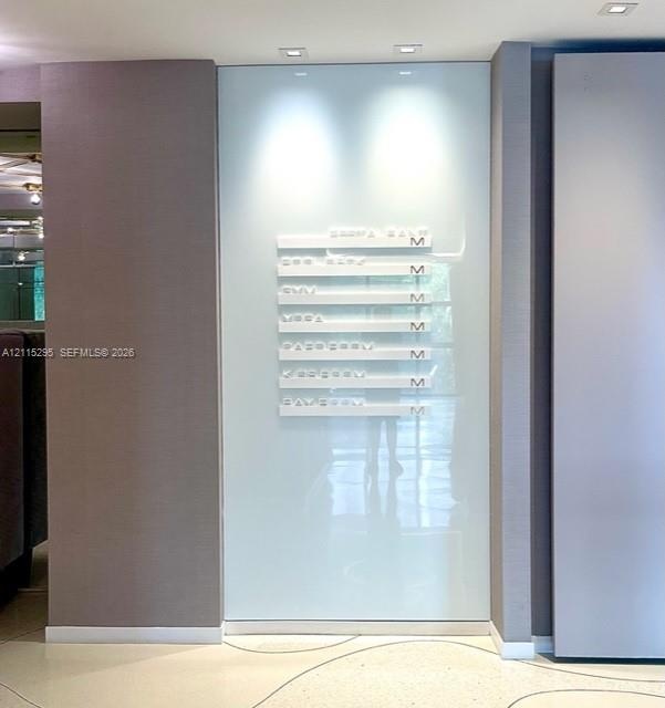 Wall-mounted directory signage featuring white tiered lettering against a backlit, floor-to-ceiling glass panel, set within a neutral-toned alcove wit