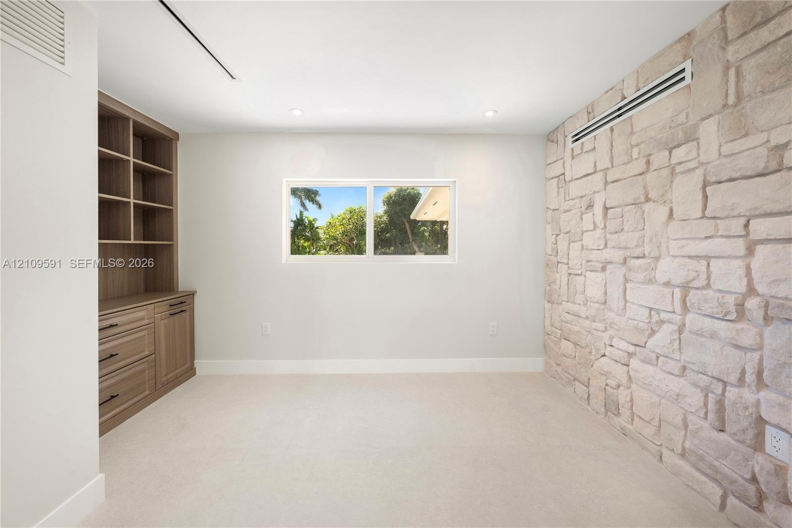 Stone accent wall, built-in wooden cabinetry featuring drawers and shelving, and a horizontal window with exterior greenery