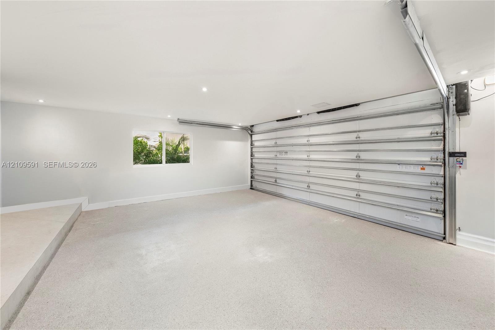 Garage interior featuring a seamless epoxy floor finish, recessed ceiling lighting, a white sectional garage door, and a single-pane window