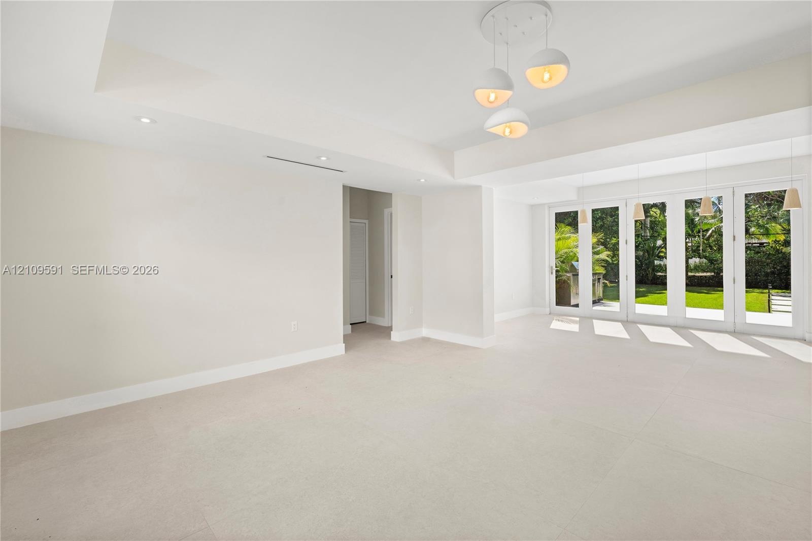 Large-format tile flooring, tray ceilings with recessed lighting, multi-globe pendant light fixture, and floor-to-ceiling glass panel doors