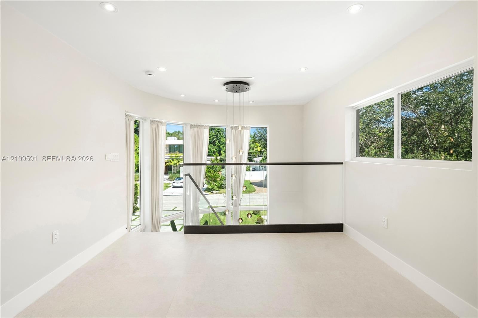 Open-concept landing featuring recessed lighting, a multi-pendant light fixture, glass railings with dark-finished metal handrails, and expansive wind