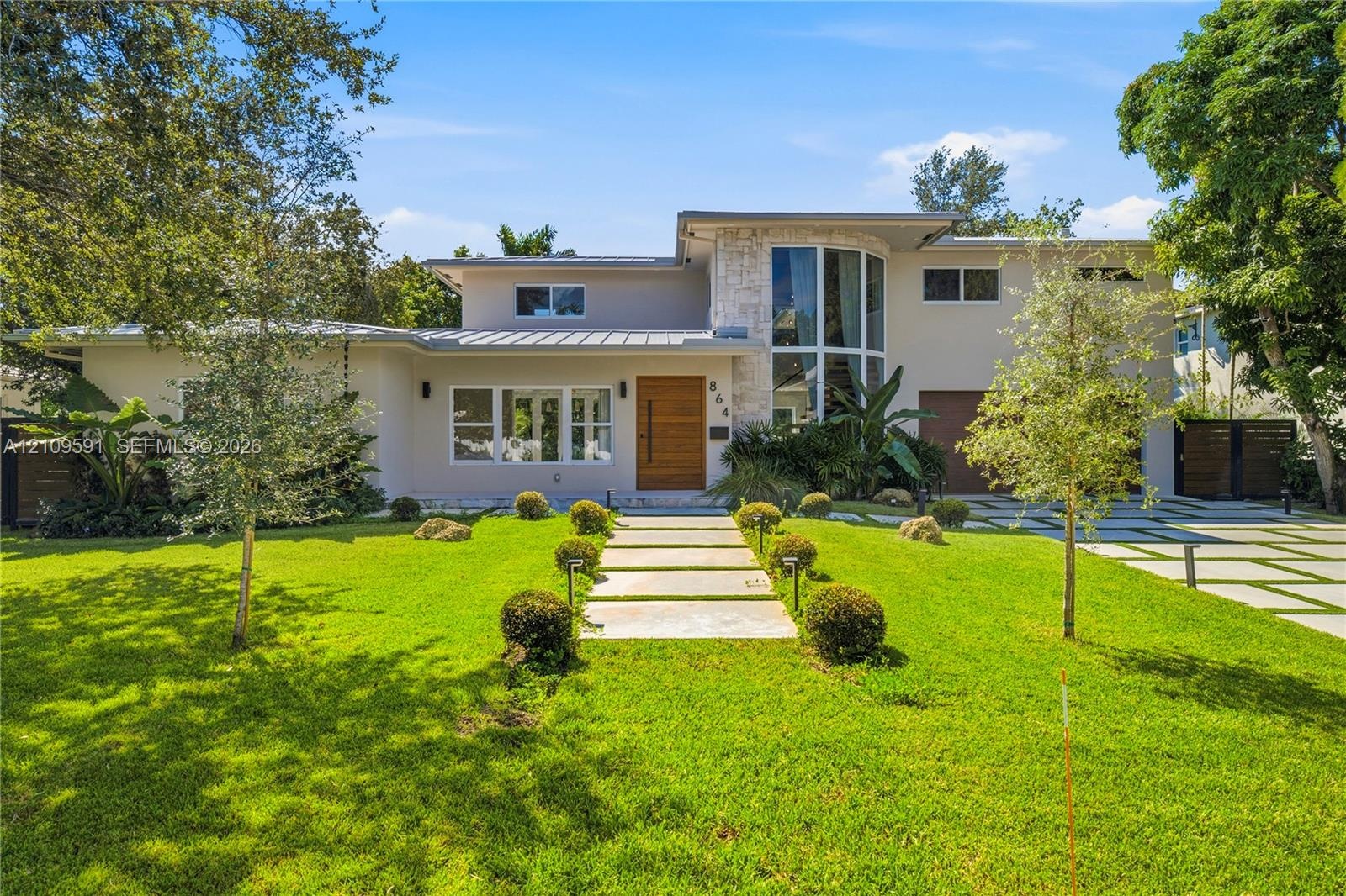 Modern exterior featuring a metal roof, stone facade accents, expansive floor-to-ceiling windows, a wood-finish front door, and a geometric concrete p