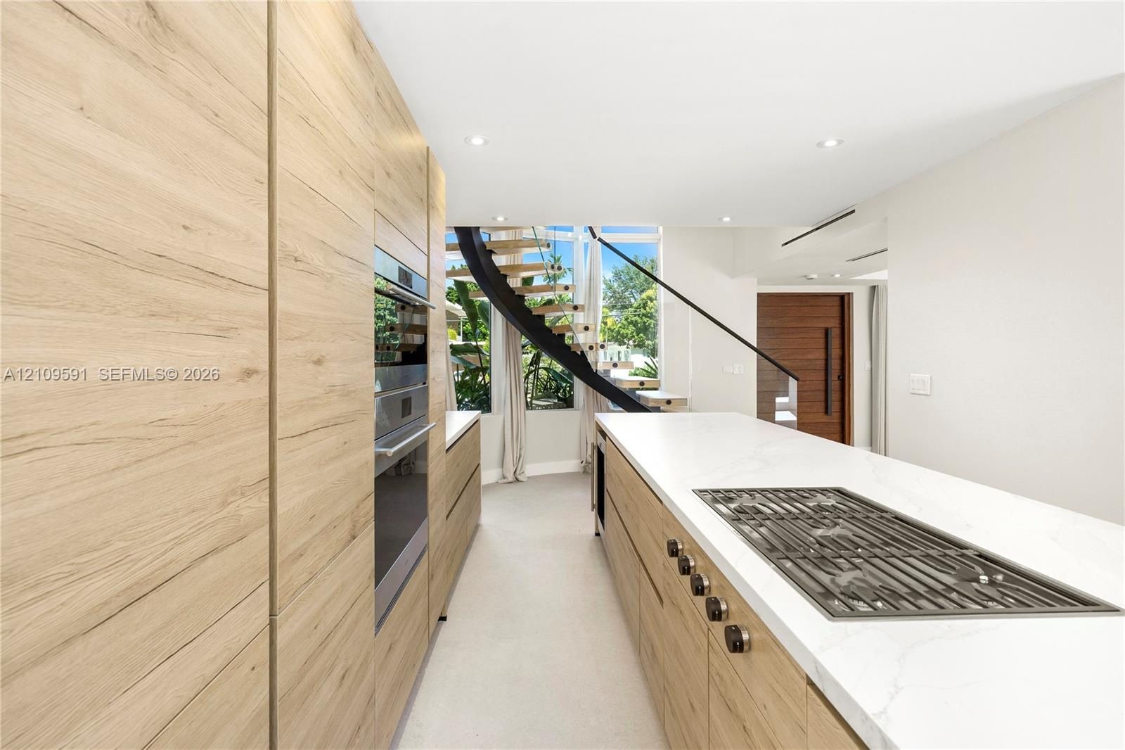 Kitchen featuring full-height wood-finish cabinetry, integrated wall oven, large island with quartz-style countertop, inset gas cooktop, and a curved 