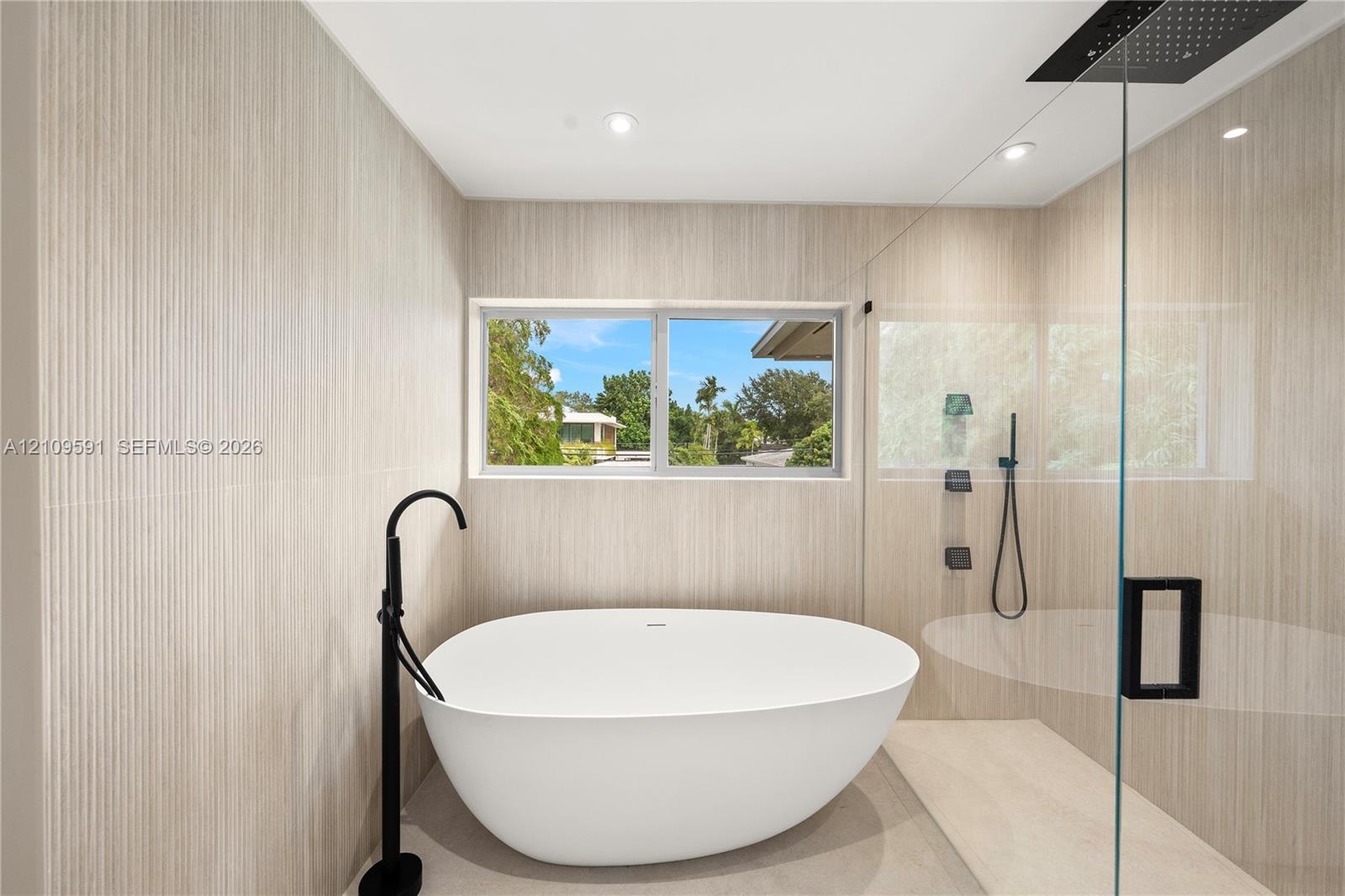 Freestanding soaking tub with matte black floor-mounted faucet, walk-in shower with glass enclosure, rain shower head, and floor-to-ceiling textured t