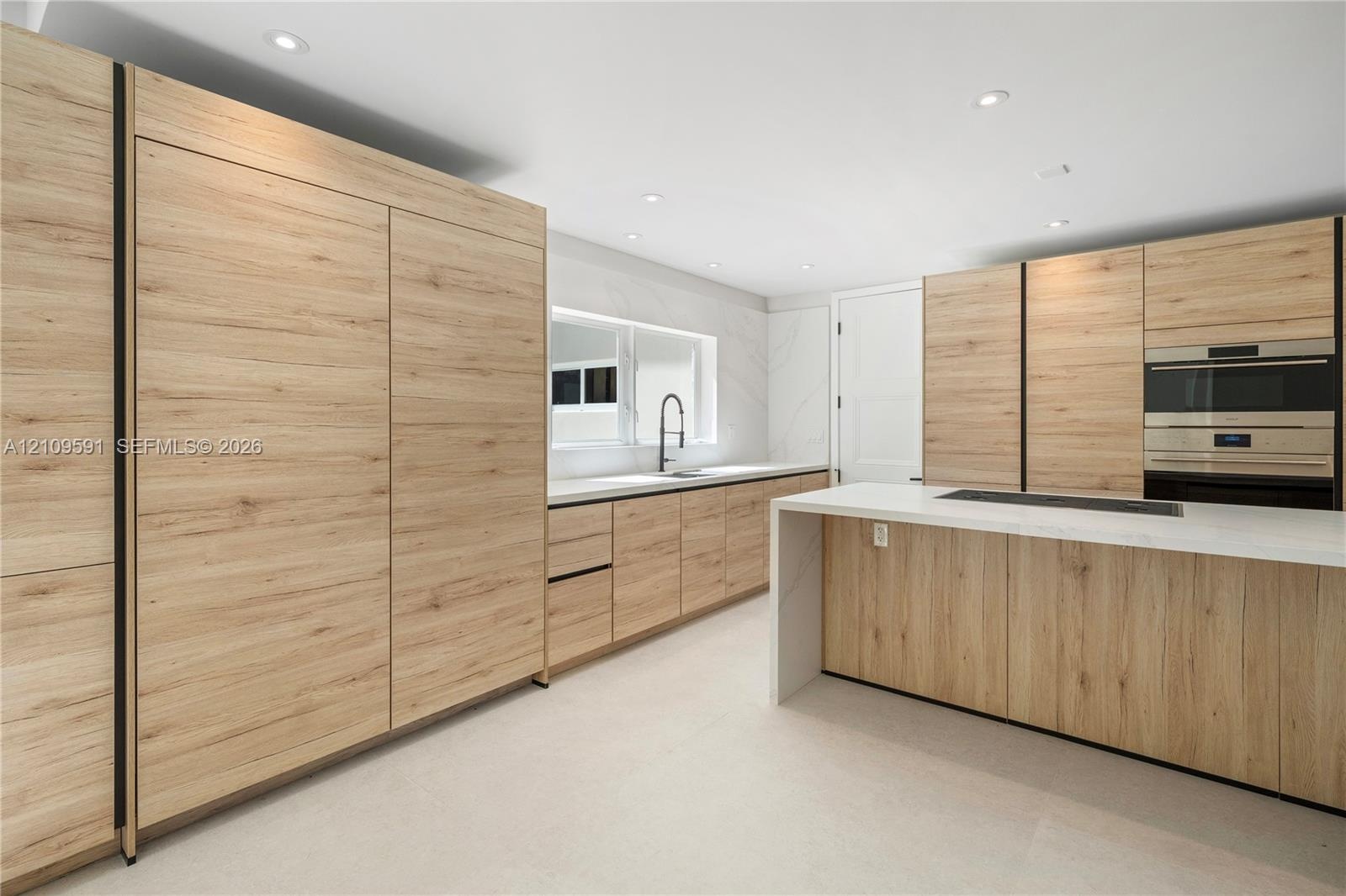 Kitchen featuring wood-finish cabinetry, a waterfall-edge island with countertop, recessed lighting, a built-in wall oven, and a single-basin sink wit