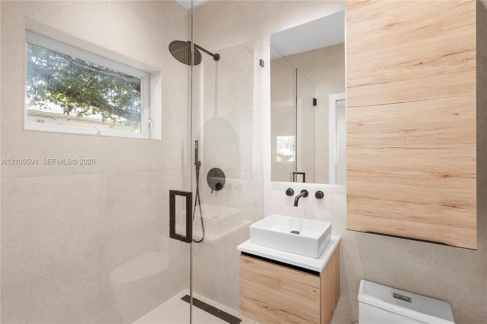 Modern bathroom featuring large-format wall tiling, a floating wood-finish vanity with a rectangular vessel sink, matte black hardware, and a glass-en