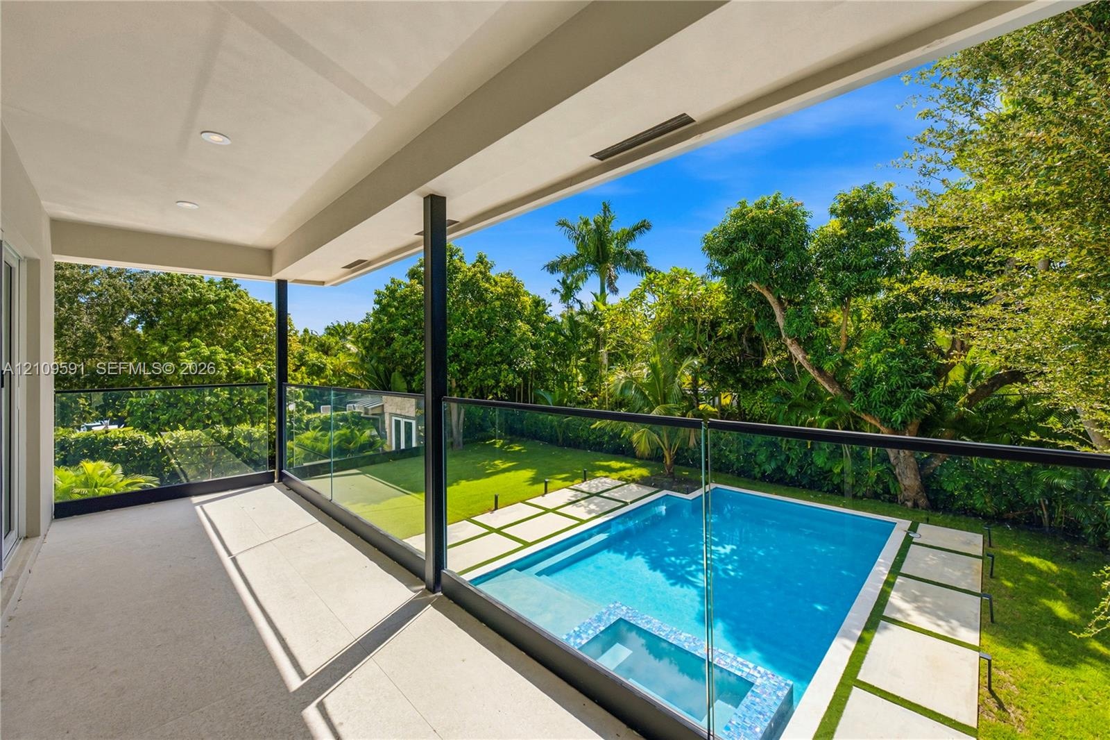 Covered balcony featuring recessed lighting and a frameless glass railing overlooking a swimming pool with an integrated spa, stone paver decking, and