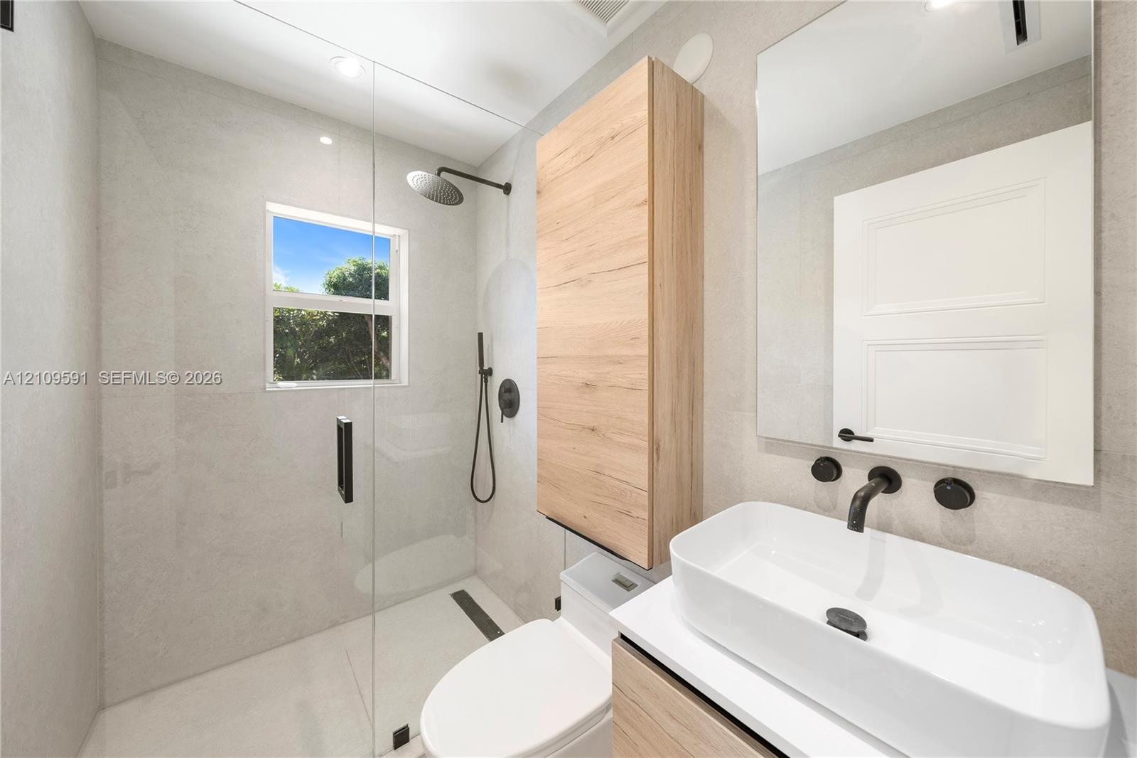 Walk-in shower with a glass enclosure and wall-mounted matte black rainfall shower head, wood-finish wall-mounted cabinetry, wall-mounted rectangular 