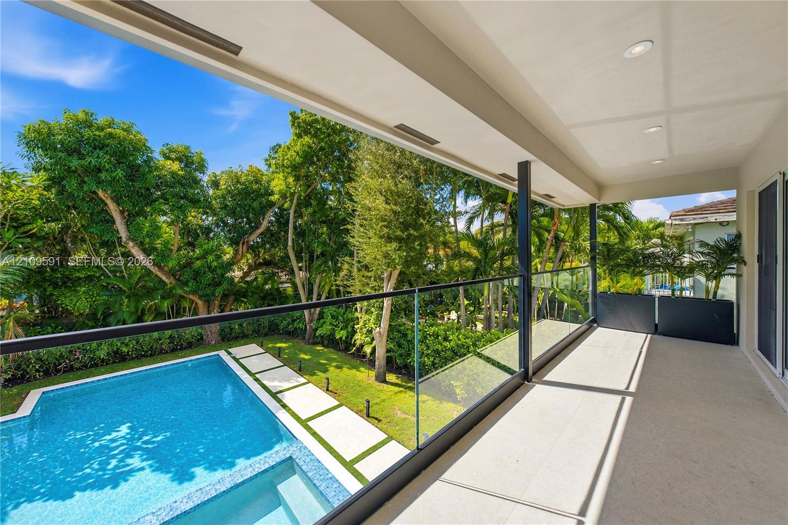 Covered balcony featuring a frameless glass railing, recessed ceiling lighting, swimming pool with integrated spa, concrete paver path, and mature lan