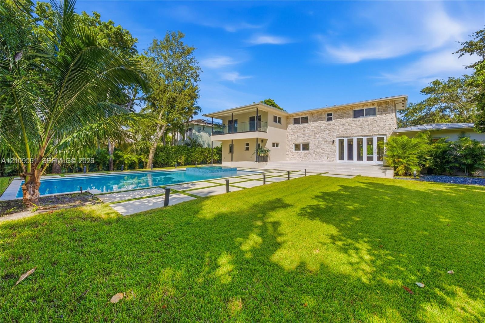 Exterior facade featuring natural stone veneer, in-ground swimming pool with integrated spa, manicured lawn, tiered patio, and second-story balcony wi