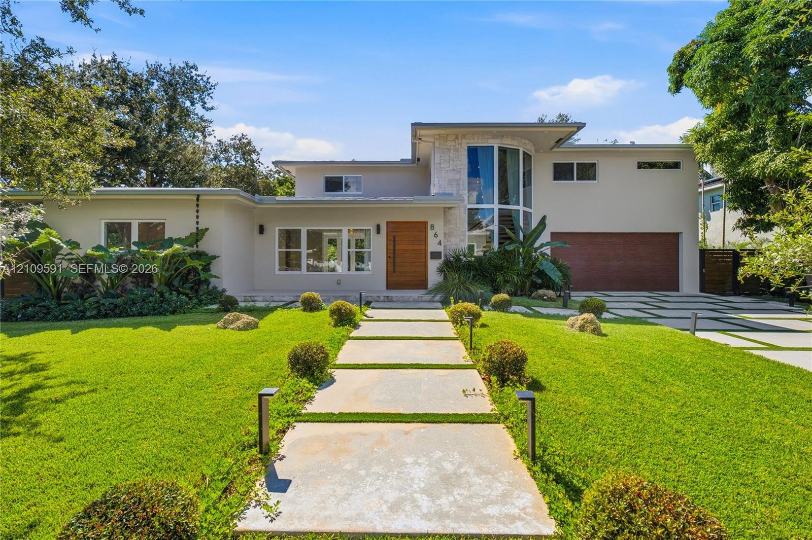 Modern exterior featuring a prominent two-story glass tower, custom horizontal wood-paneled entry door, geometric concrete paver walkway, and stone ac