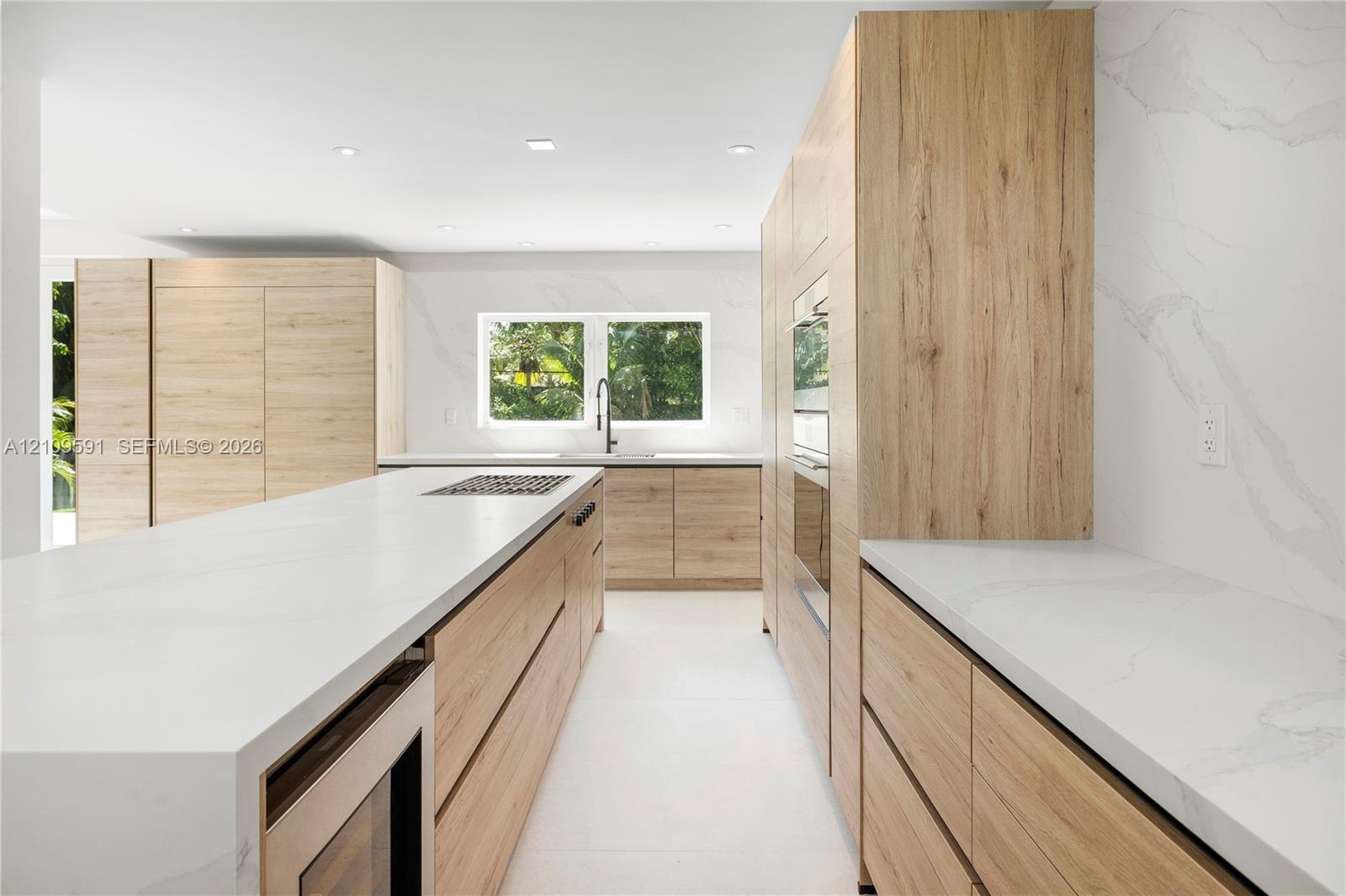 Kitchen featuring light wood-finish cabinetry, quartz countertops with full-height backsplash, a large center island, built-in stainless steel applian