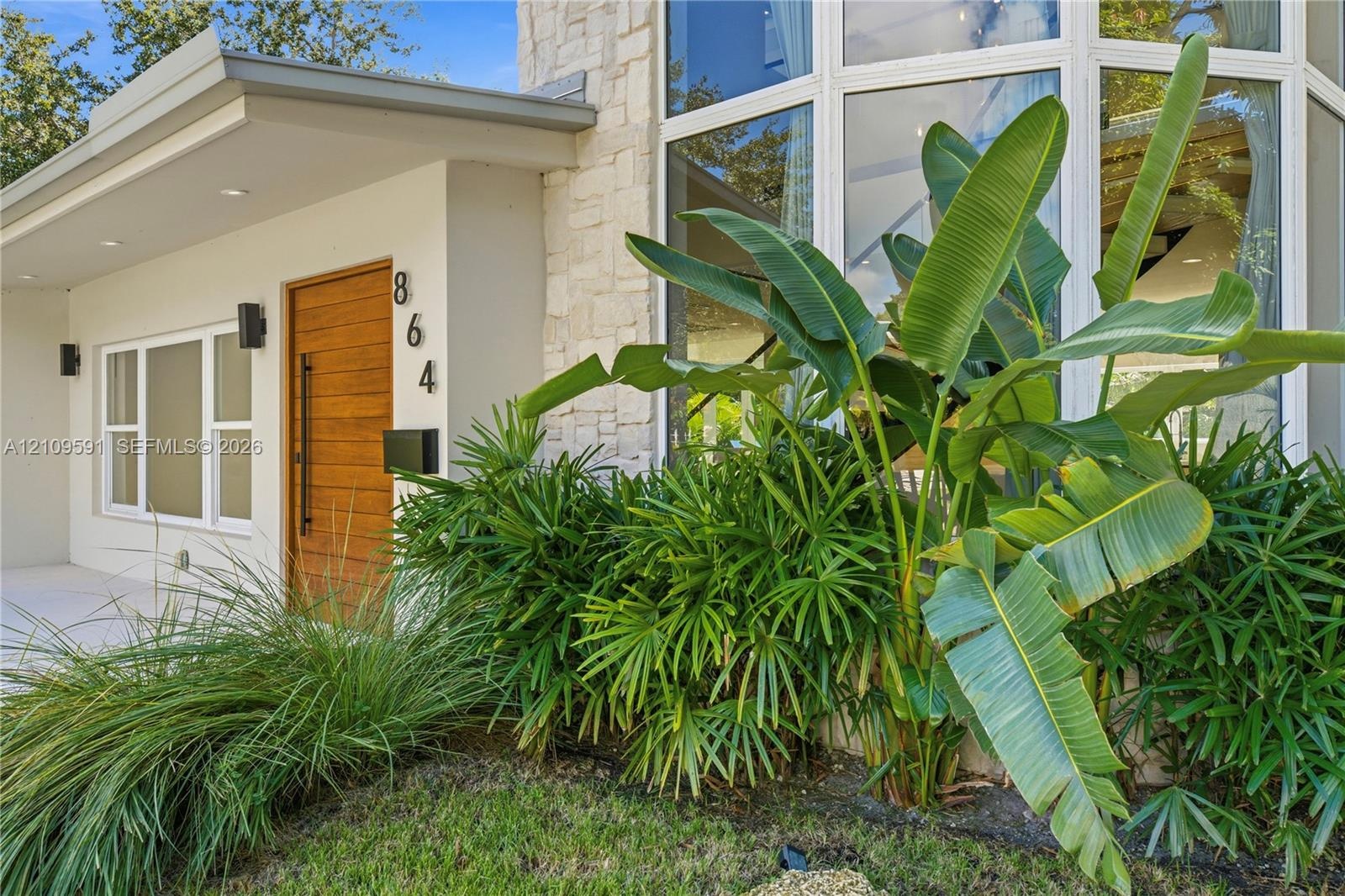 Modern facade featuring a natural stone accent wall, expansive multi-pane windows, and a horizontal wood-grain door with a vertical matte black pull h