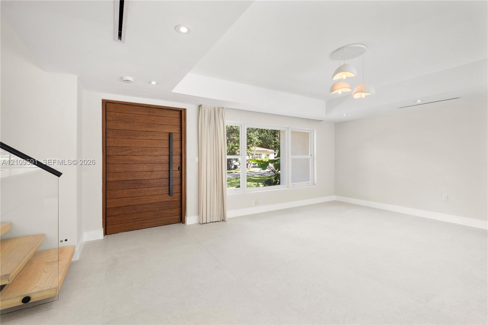 Horizontal wood-plank entry door with a vertical matte black pull handle, recessed ceiling lighting, three-globe pendant fixture, and glass-panel stai