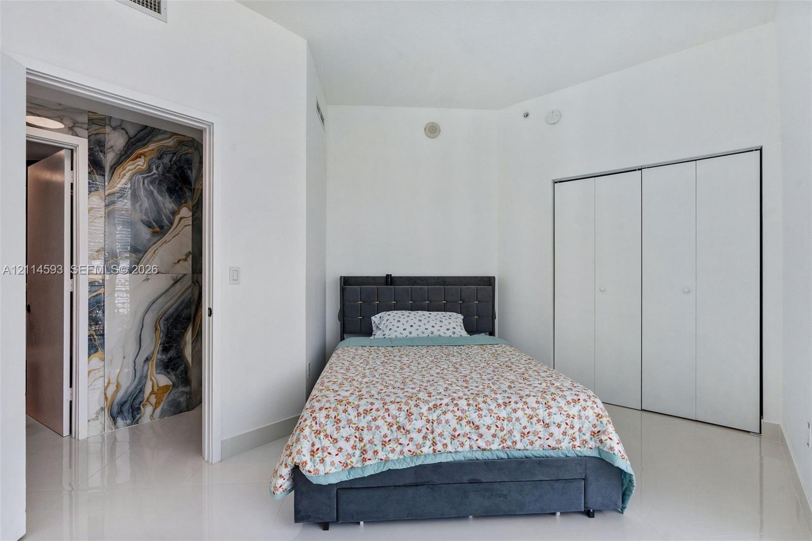Neutral-toned interior space featuring polished tile flooring, built-in floor-to-ceiling wardrobe with white panel doors, and distinctive wall tilewor