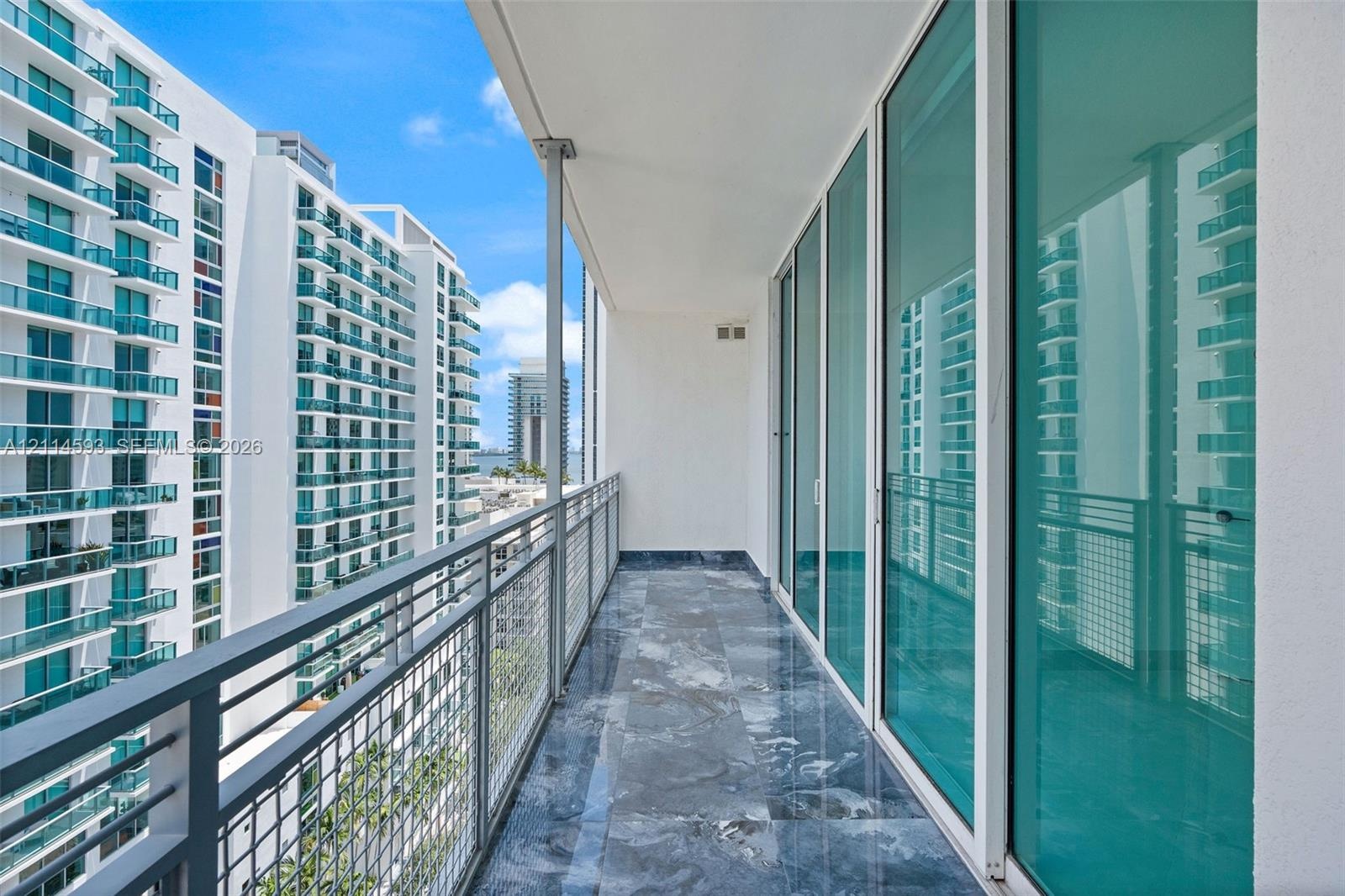 Private covered balcony with stone-finish flooring, full-height glass panel walls, and metal mesh railing