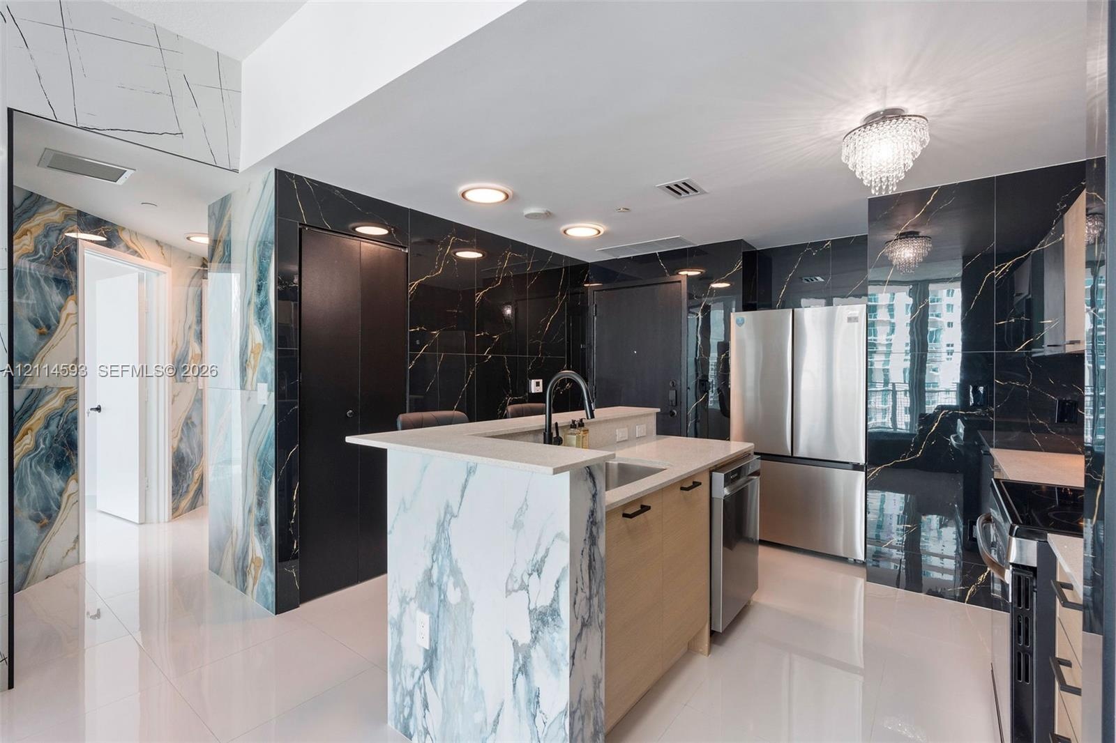 Kitchen featuring a center island with light stone-finish waterfall counters, high-gloss dark stone wall cladding, stainless steel appliances, and pol