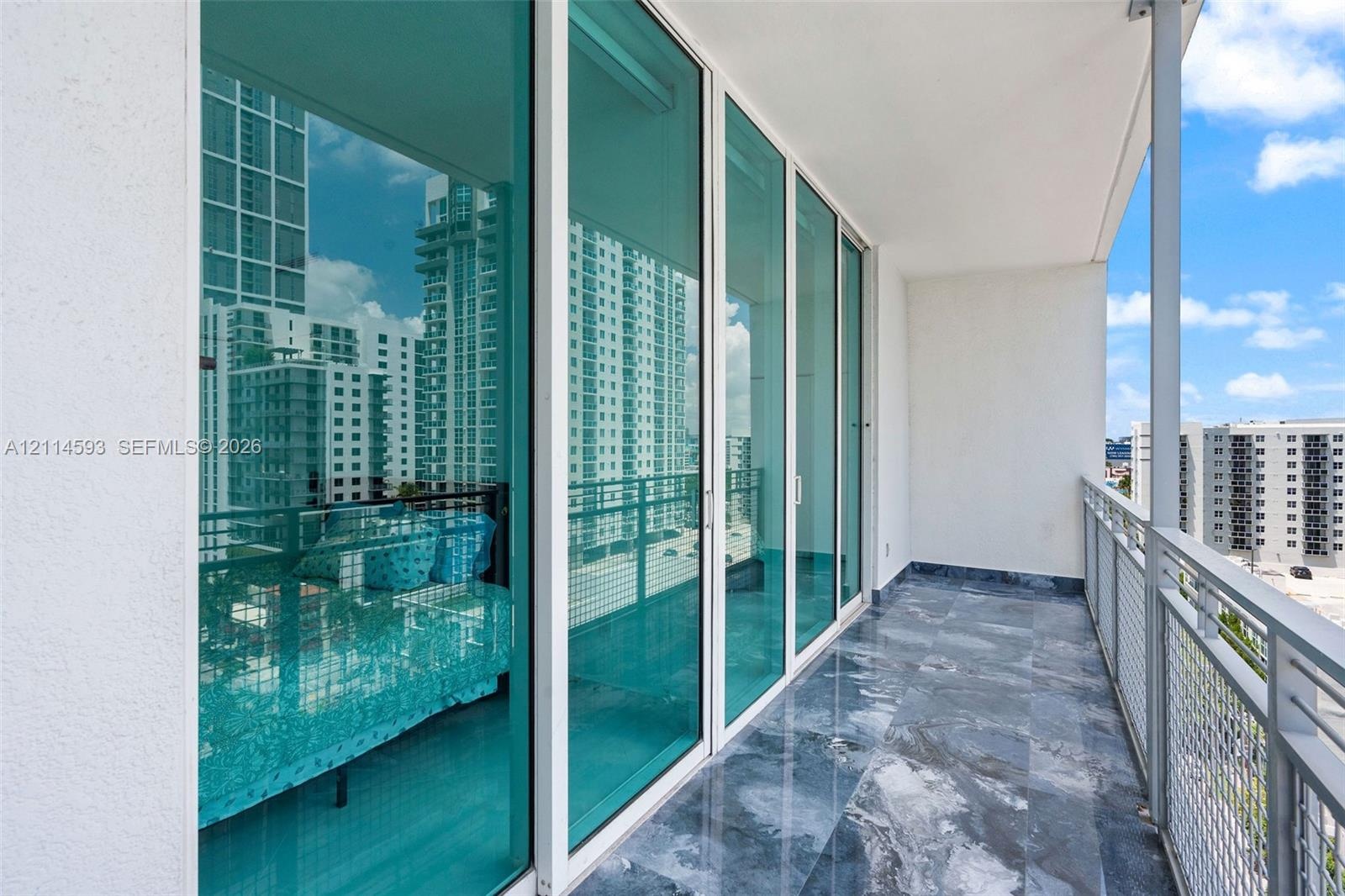 Covered balcony featuring stone-tiled flooring, white metal railing, and expansive floor-to-ceiling glass sliding doors