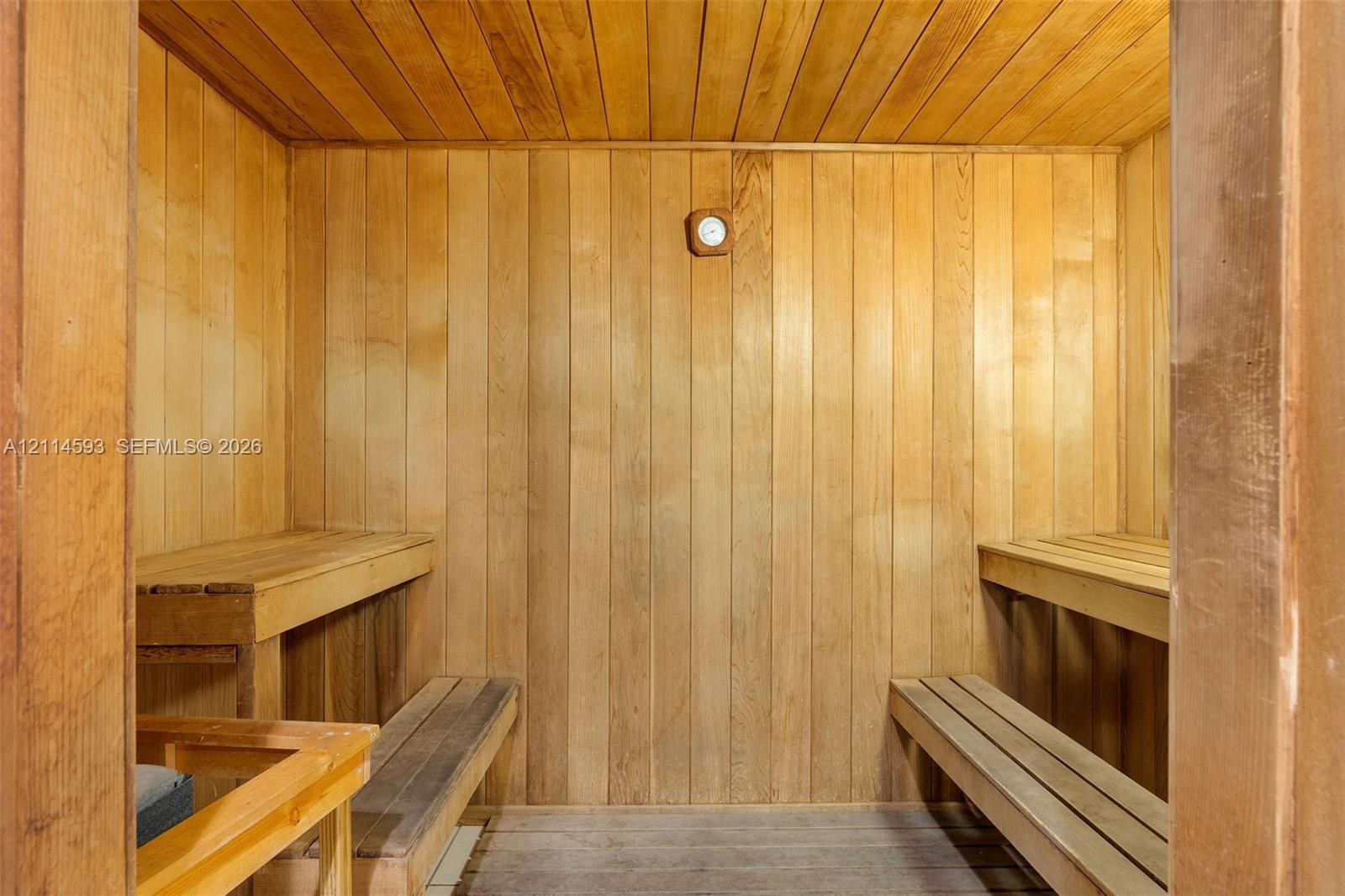 Sauna featuring natural wood-paneled walls and ceiling, multi-level slatted wooden benches, and wall-mounted analog thermometer