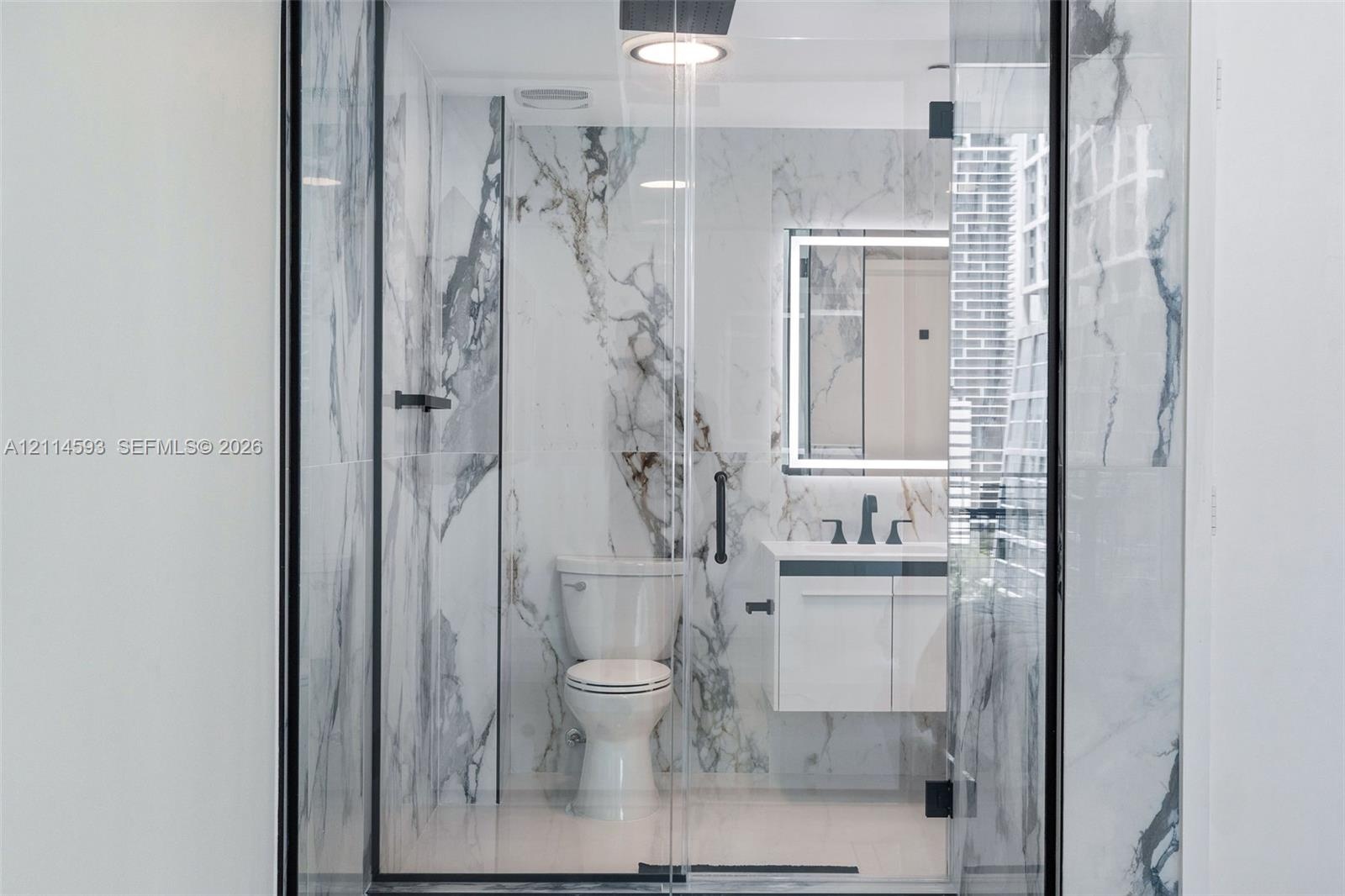 Full-height stone-patterned wall tile, floating vanity with integrated countertop, wall-mounted rectangular mirror with perimeter LED lighting, matte 
