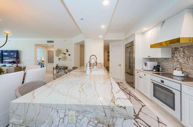 Custom Cucina with a Grand Peninsula, Quartzite Counter & Backsplash Accessorized Stainless Appliances.